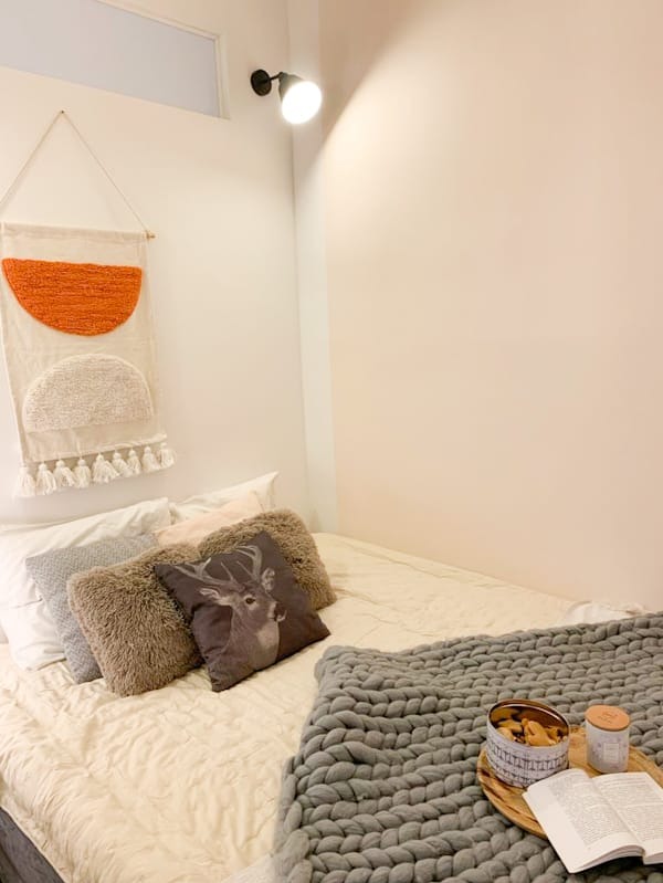 Przytulna aranżacja sypialni w Krakowie: miękkie poduszki, gruby koc, dekoracje ścienne i lampa, tworzące ciepłą atmosferę w pokoju.
