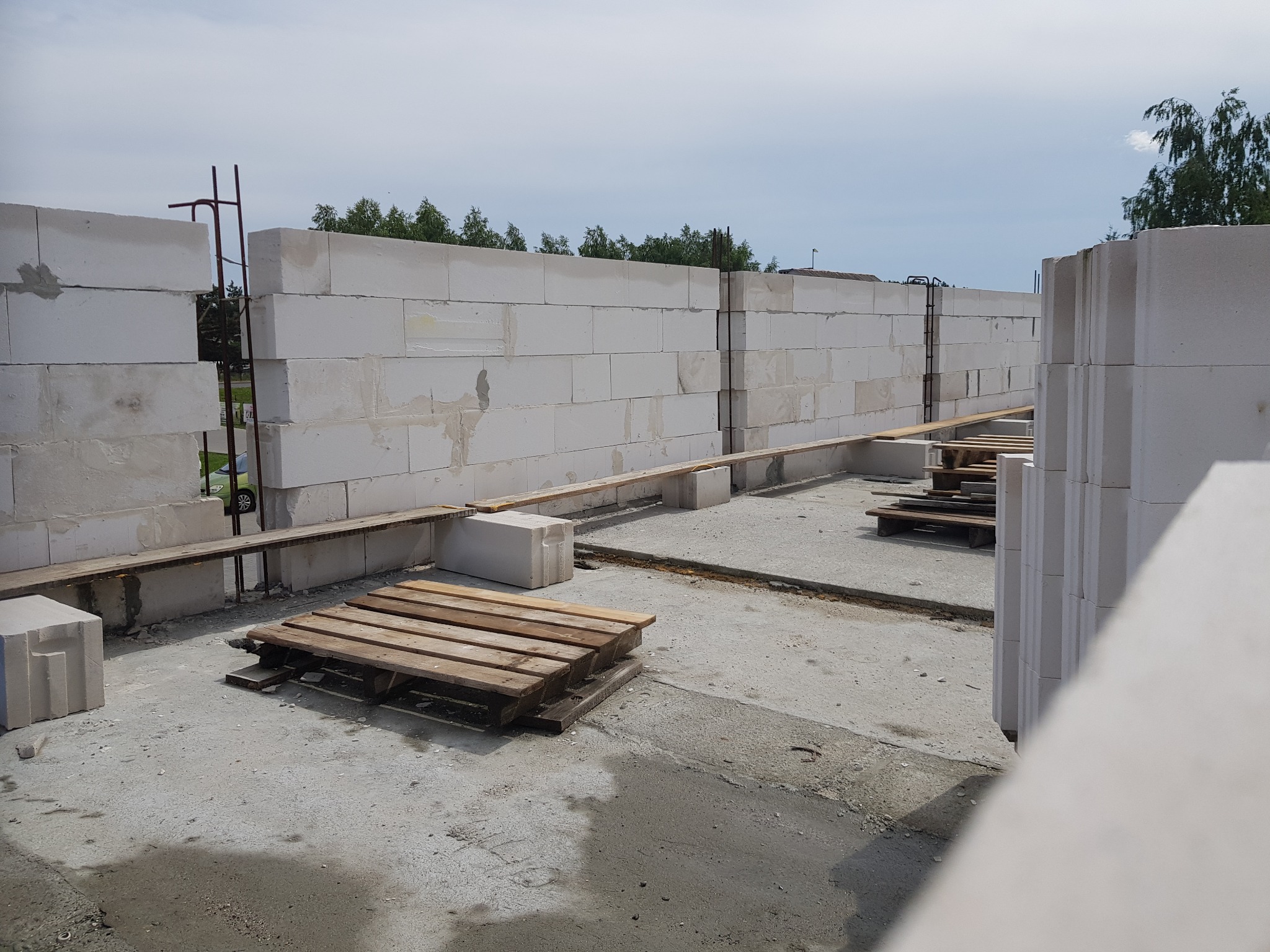 Wznoszenie ścian z bloczków betonowych zbrojonych pionowo stalą w Kcyni, widoczne drewniane palety i deski na podłożu.