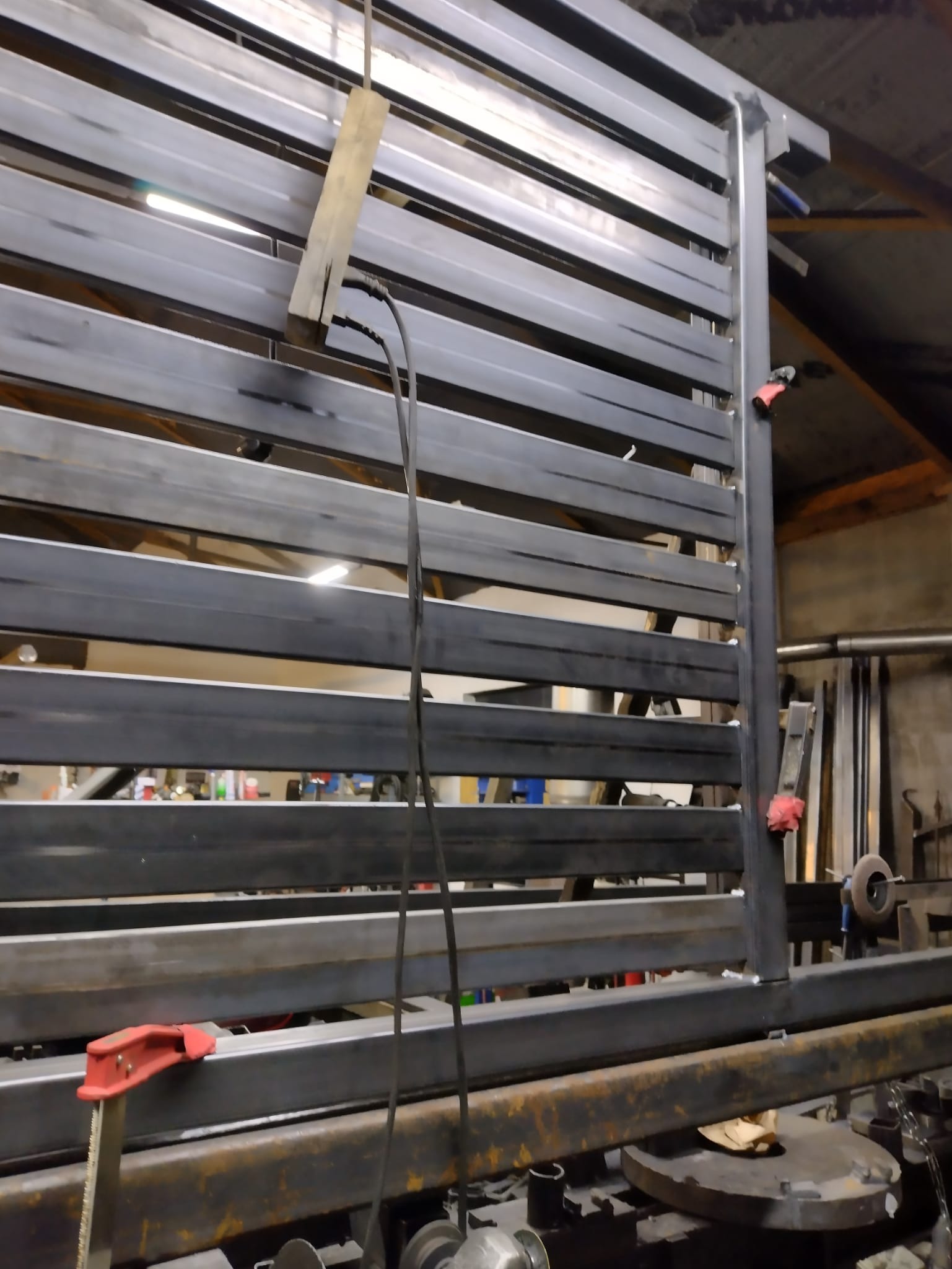 Konstrukcja bramy przemysłowej w trakcie spawania, widoczne poziome profile stalowe, elementy mocujące i przewody spawalnicze.