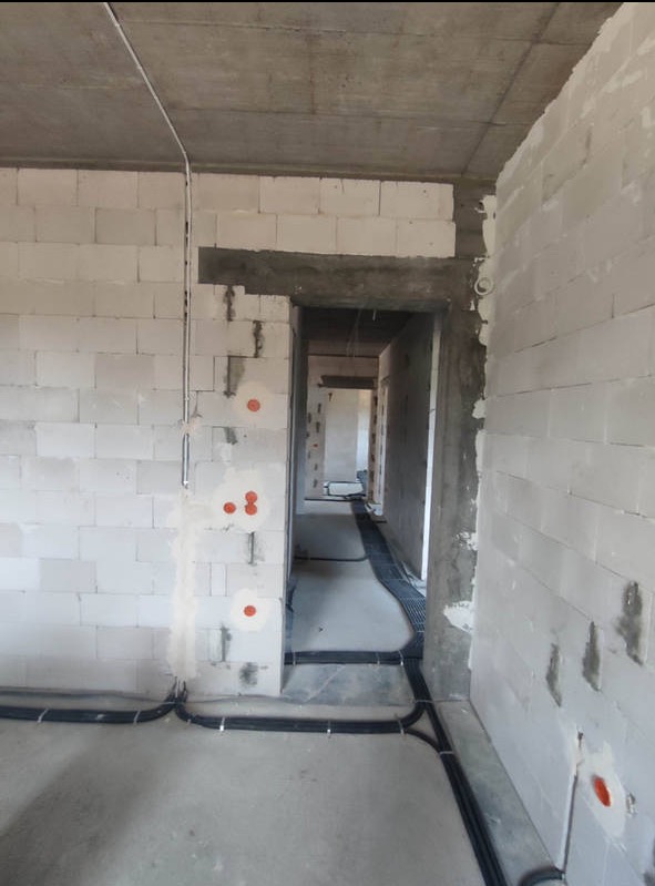 Surowy stan budynku w Olsztynie z widoczną instalacją elektryczną w peszlach na podłodze i przygotowanymi punktami na ścianach z białego bloczka.