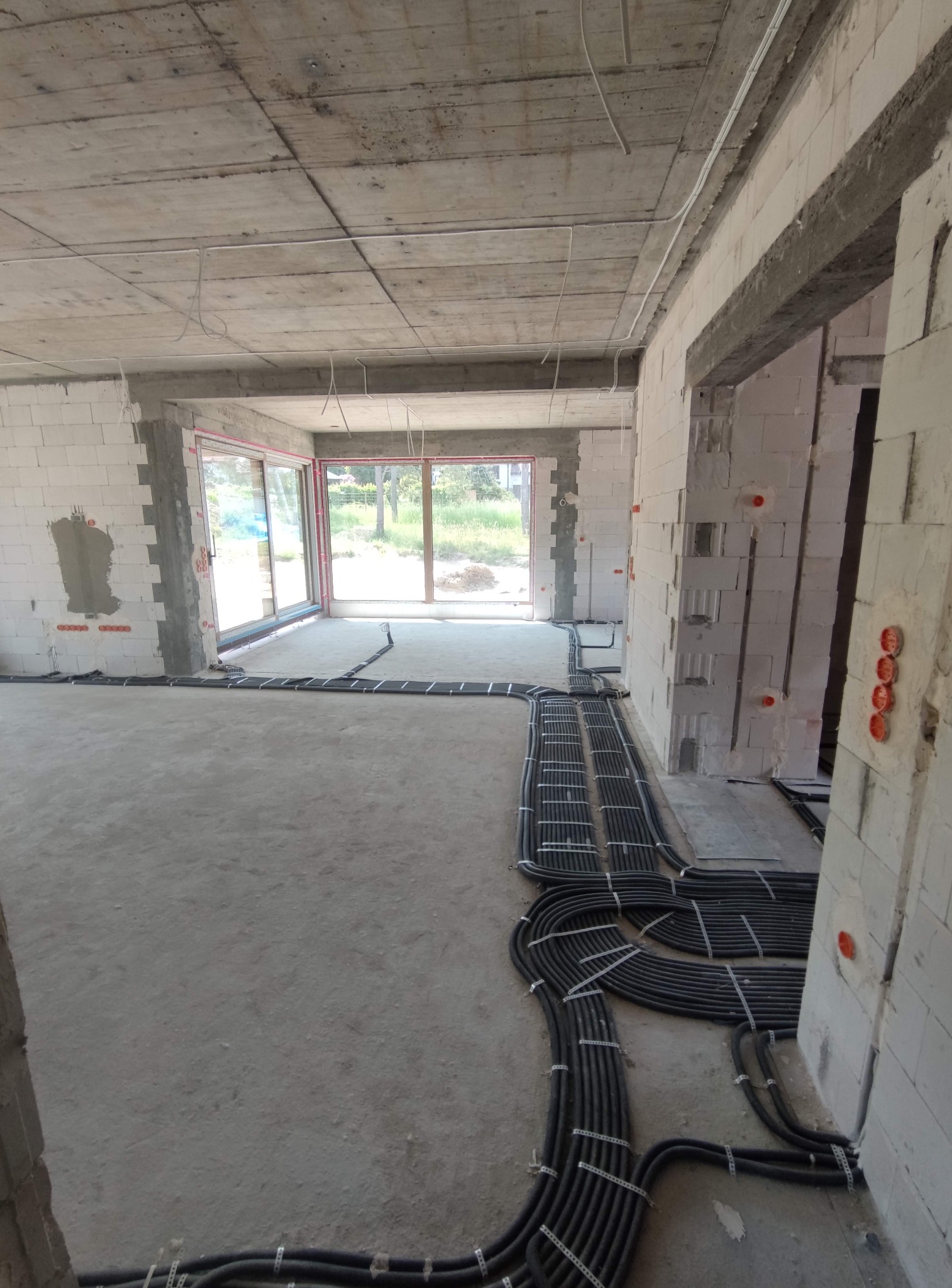 Surowy stan: czarne rury instalacji elektrycznej ułożone na podłodze w nowym budynku z białego betonu komórkowego, widoczne puszki elektryczne w ścianach.