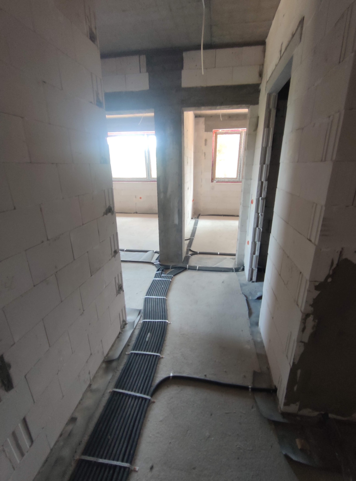 Wnętrze w trakcie budowy z widoczną wiązką przewodów elektrycznych ułożoną wzdłuż ściany, prowadzącą przez kilka pomieszczeń. Surowy stan wykończenia.