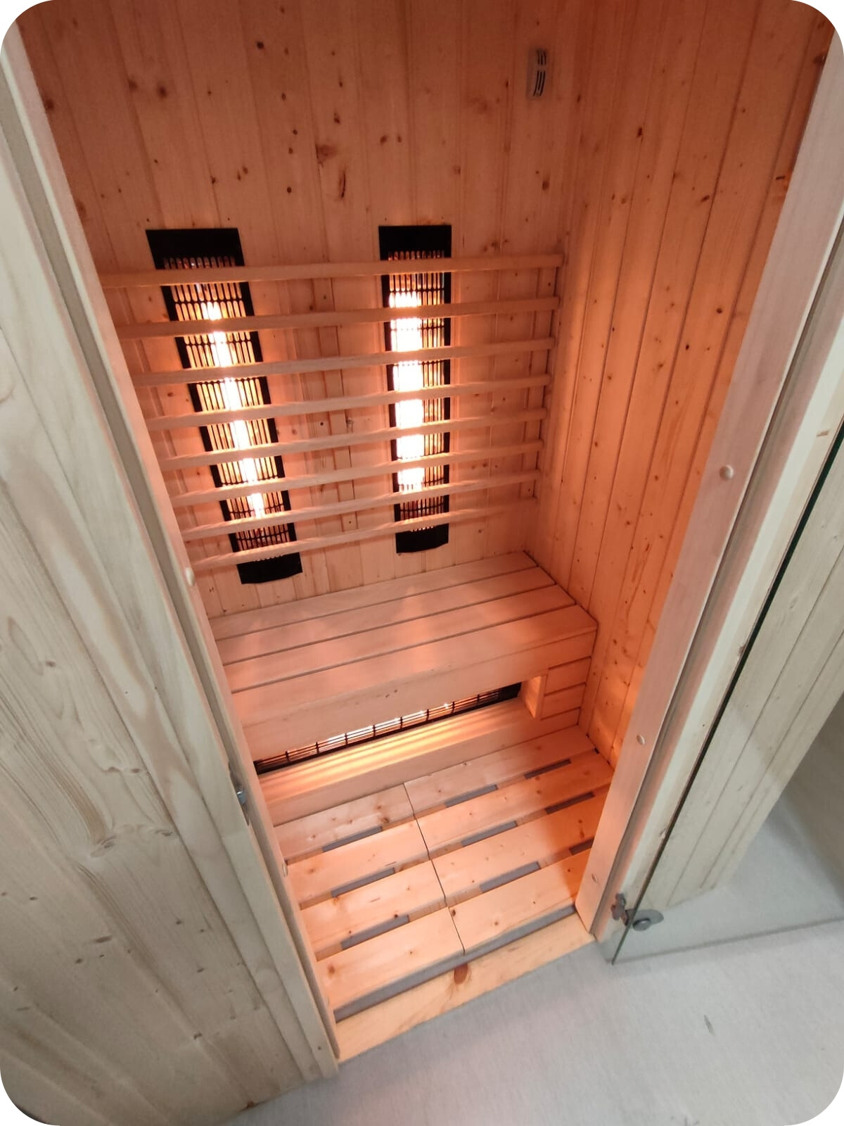 Wnętrze sauny z drewnianą ławką i panelami grzewczymi, widok od wejścia.