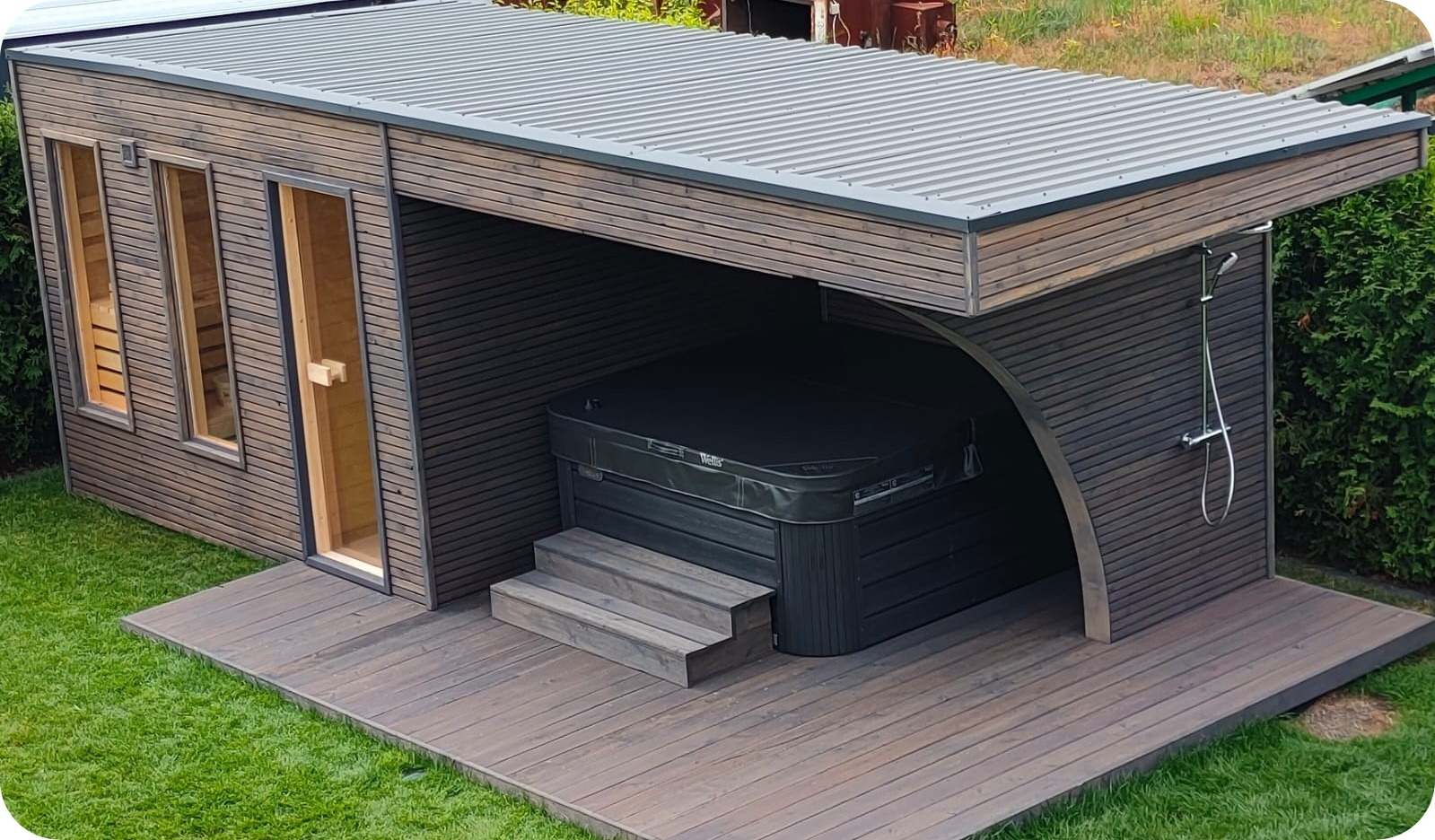 Nowoczesna, drewniana konstrukcja z zadaszeniem kryjąca jacuzzi i prysznic zewnętrzny, z sauną z trzema oknami po lewej stronie, na drewnianym tarasie i trawniku.