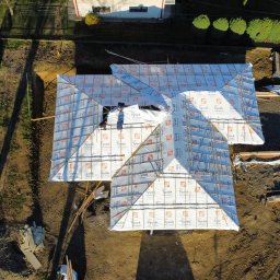 JD&KS SPÓŁKA Z OGRANICZONĄ ODPOWIEDZIALNOŚCIĄ - Budowa dachu z izolacją Tyvek, widok z góry. Prace dekarskie w toku, widoczne elementy konstrukcyjne i materiały izolacyjne. Ujęcie z drona ukazuje postęp prac.