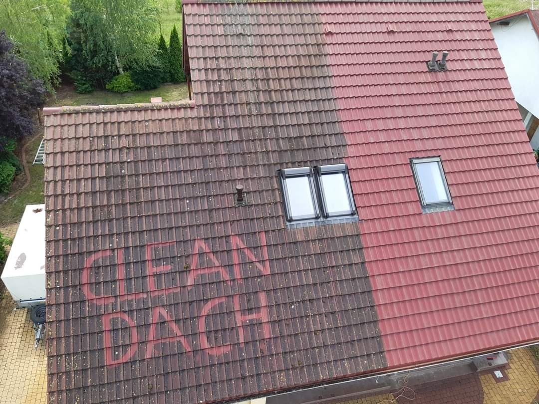 Częściowo wyczyszczony dach z czerwonej dachówki, widoczne okna dachowe i napis 'CLEAN DACH' na brudnej części dachu, obok zaparkowana przyczepa.
