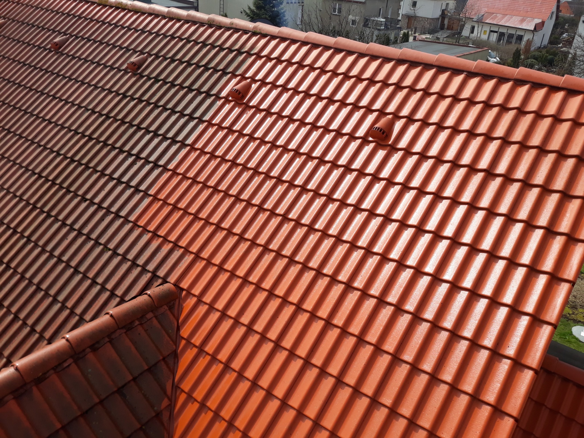 Częściowo wyczyszczony dach z czerwonej dachówki ceramicznej, widoczne kominki wentylacyjne, kontrast między czystą a zabrudzoną powierzchnią.