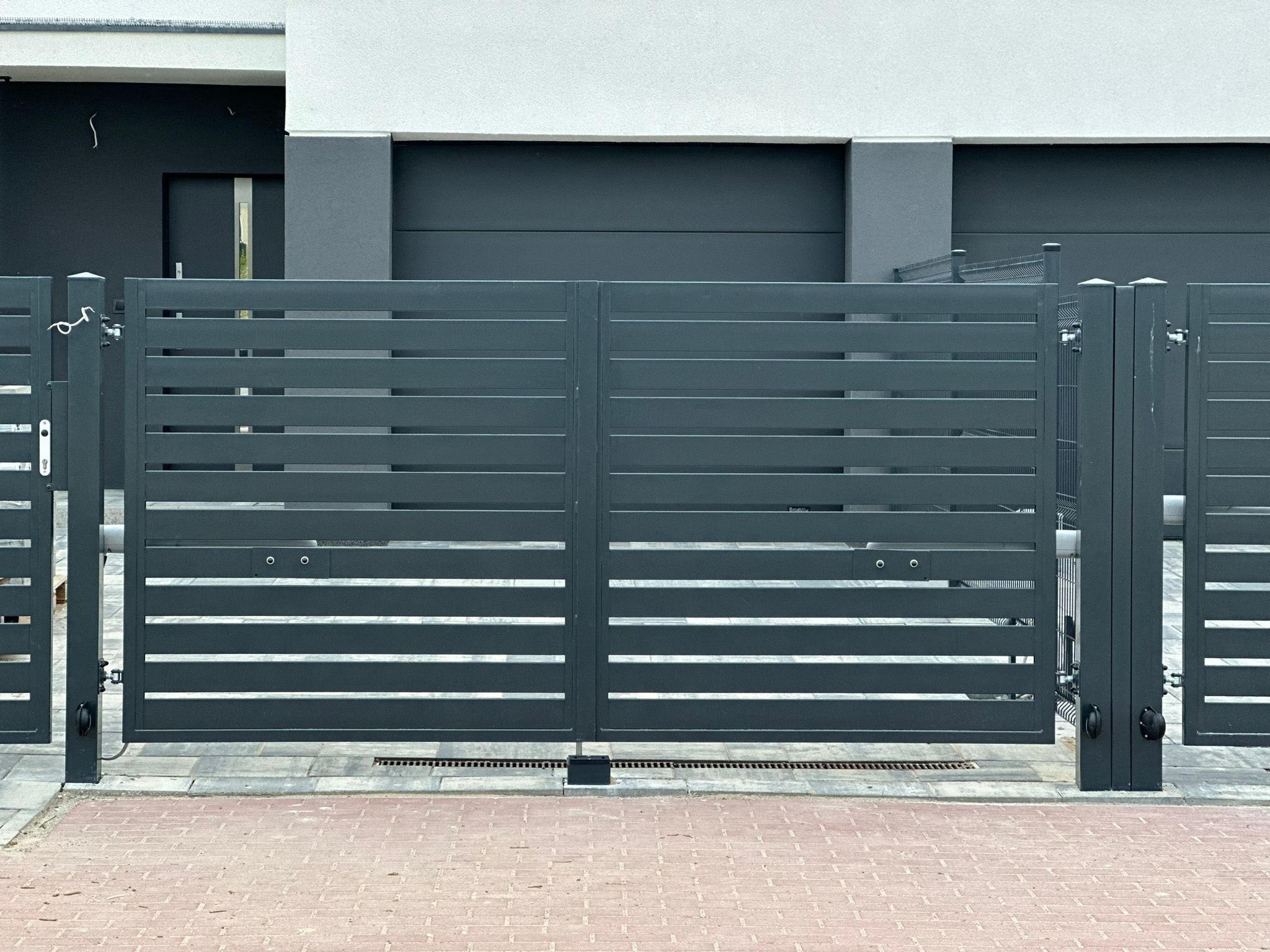 Nowoczesna, pozioma brama wjazdowa w kolorze antracytowym, z automatycznym systemem otwierania, na tle domu z garażem, wykończona czerwoną kostką brukową.