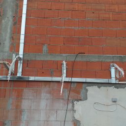 Pro-Split - Instalacja elektryczna w korytach i peszlach prowadzona po surowej ścianie z czerwonej cegły dziurawki, widoczne przewody i puszka elektryczna.