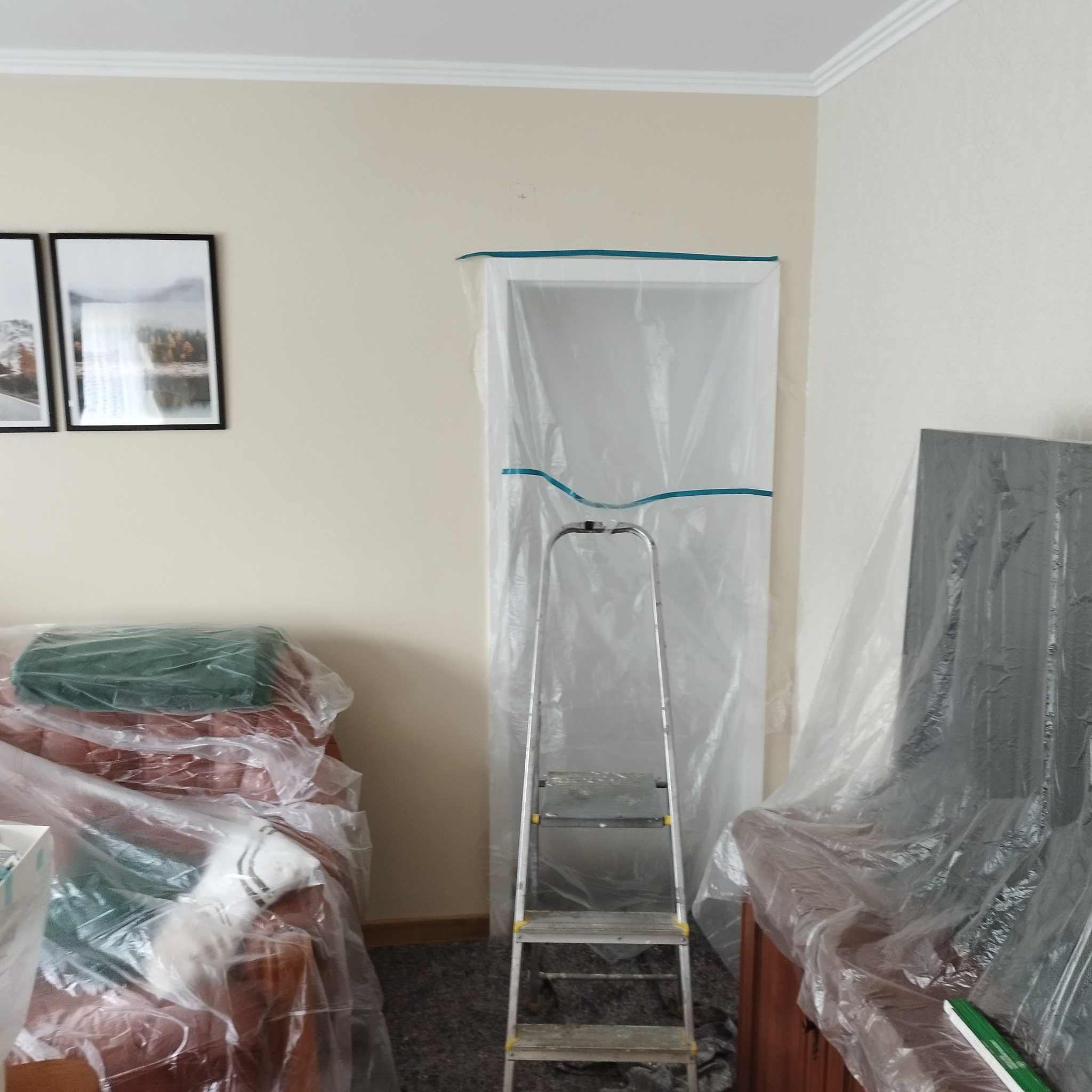 Pokój przygotowany do malowania ścian: meble i futryna drzwi zabezpieczone folią malarską, drabina aluminiowa rozstawiona przed wejściem.