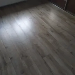 Ułożone panele podłogowe w odcieniach szarości i brązu, widoczne fragmenty ściany z grzejnikiem i szafy przesuwnej.