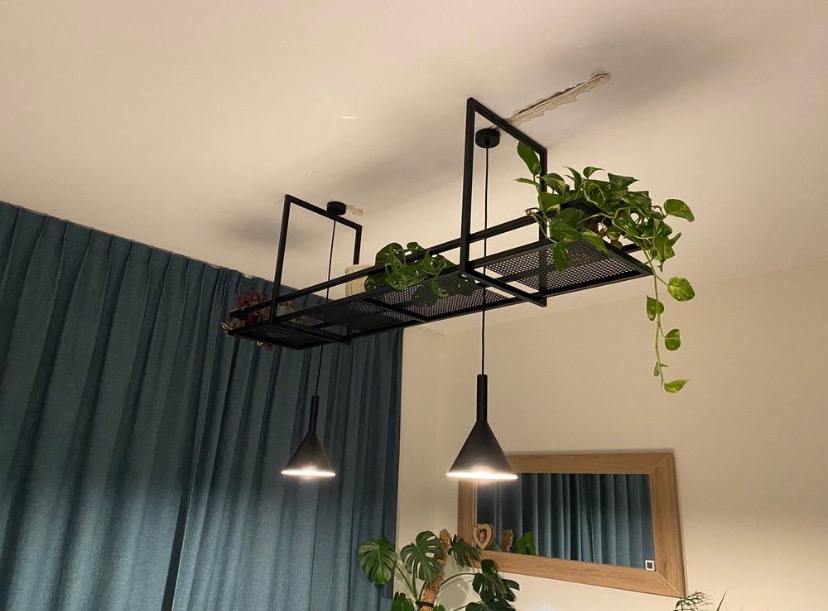 Czarna, metalowa konstrukcja podwieszona do sufitu, służąca jako kwietnik i oświetlenie, z wiszącymi lampami i roślinami w doniczkach.