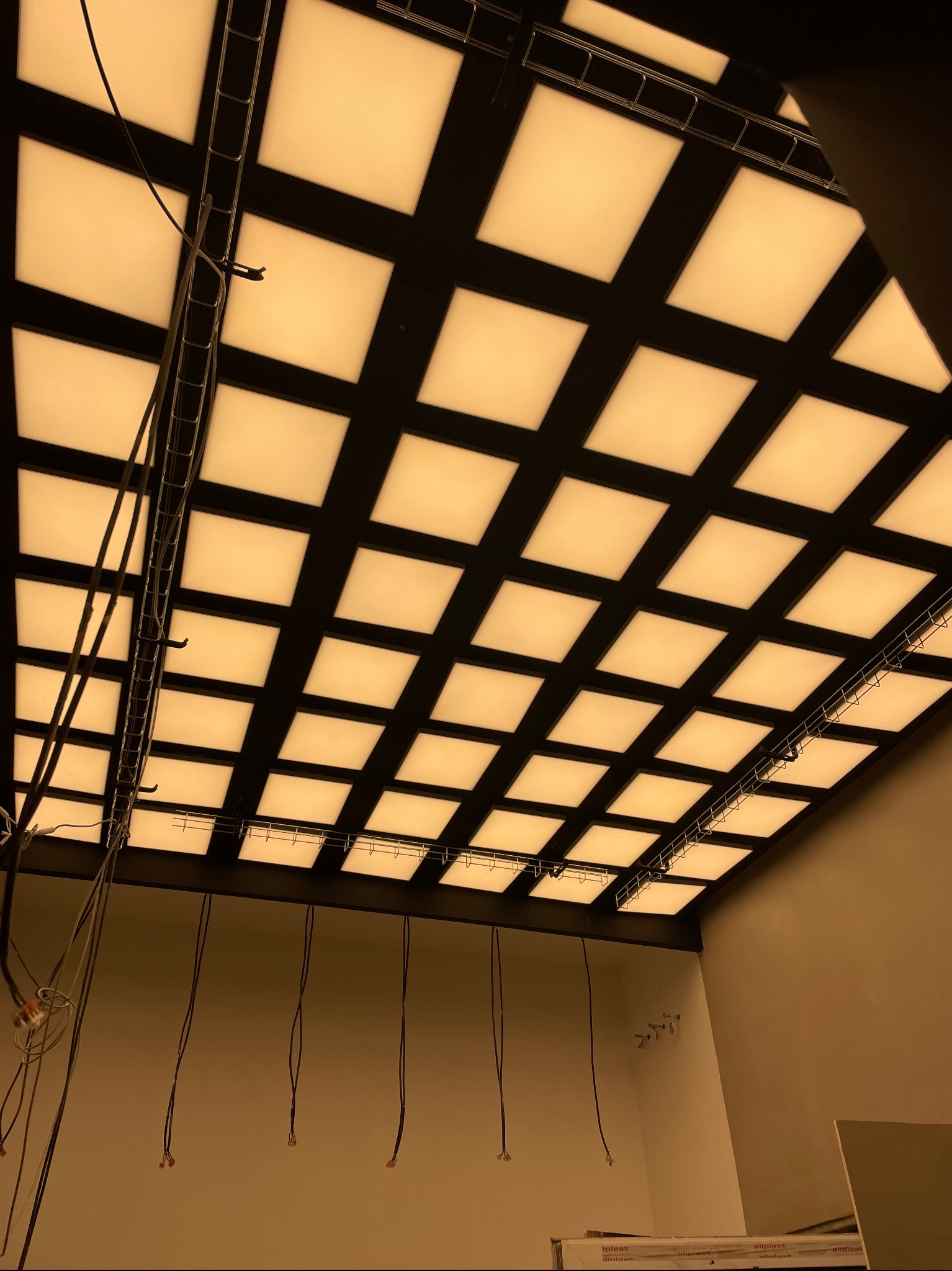 Sufit podwieszany z kwadratowymi panelami LED, widoczne kable i elementy konstrukcyjne w trakcie montażu.