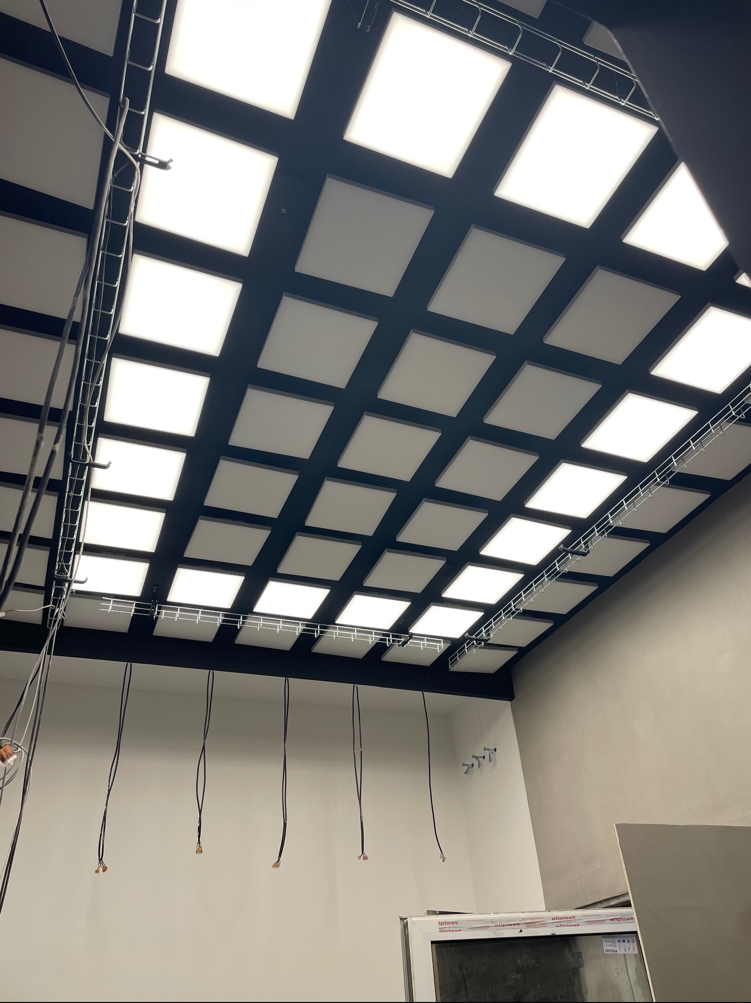 Montaż kasetonów LED w rastrze sufitowym, widoczne przewody elektryczne i elementy konstrukcyjne