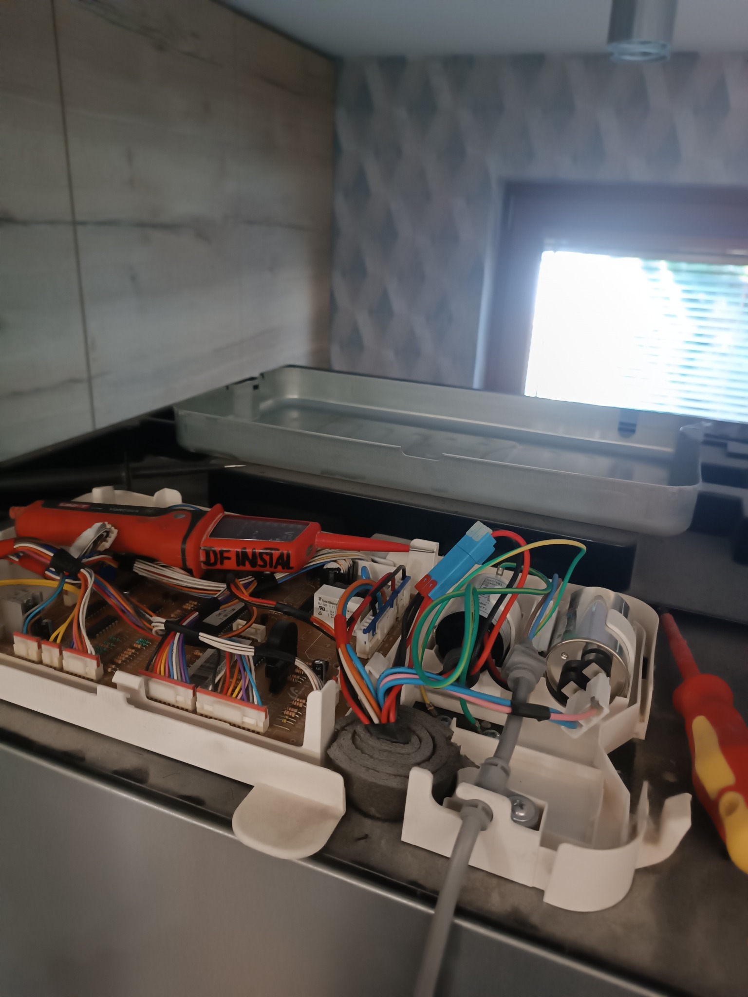 Otwarta płyta indukcyjna z widoczną elektroniką, przewodami i miernikiem napięcia z naklejką DF INSTAL.