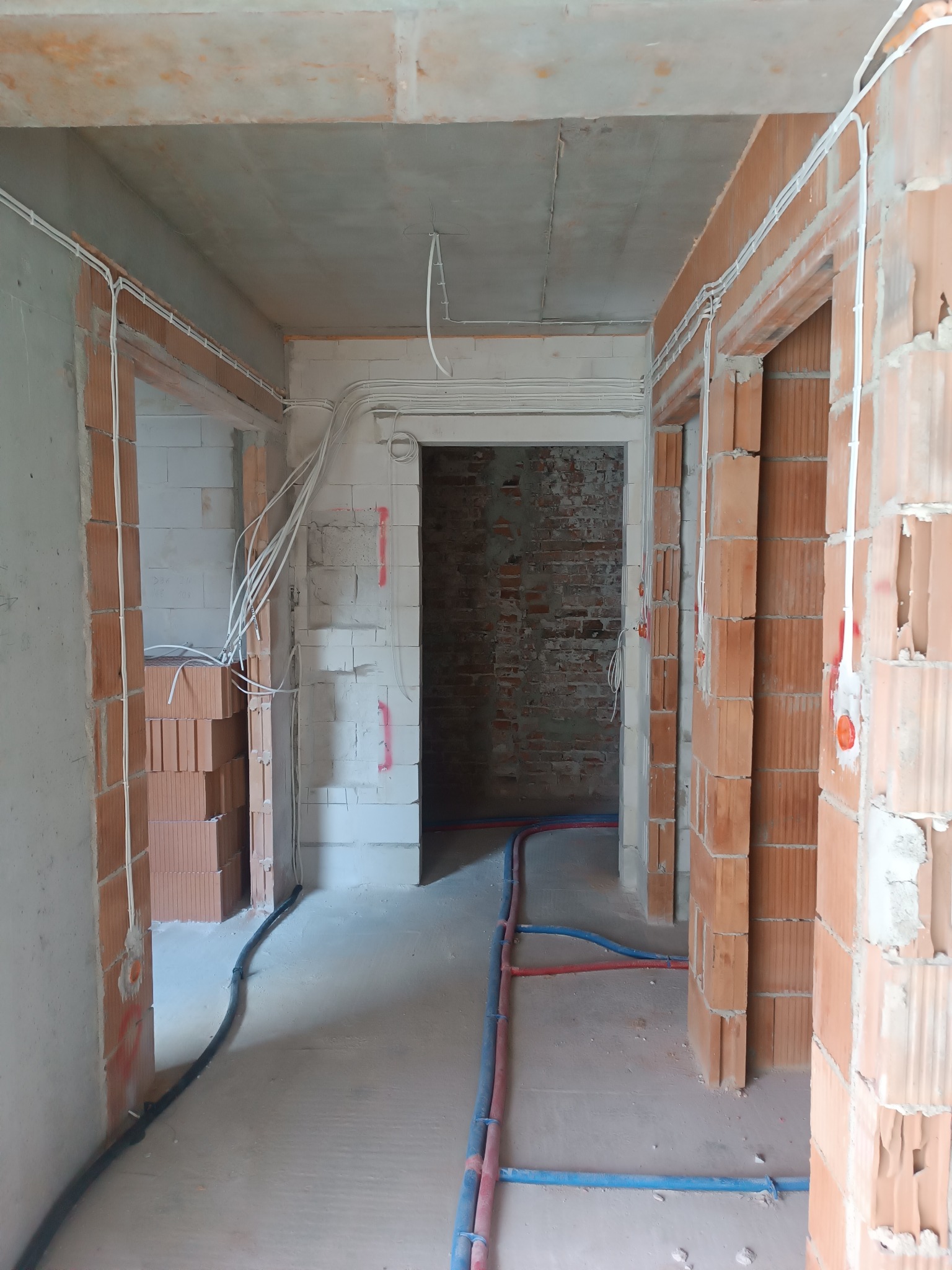 Wnętrze w trakcie remontu: widoczne przewody elektryczne prowadzone po ścianach z cegły dziurawki, instalacja wodna ułożona na podłodze, surowy betonowy strop.
