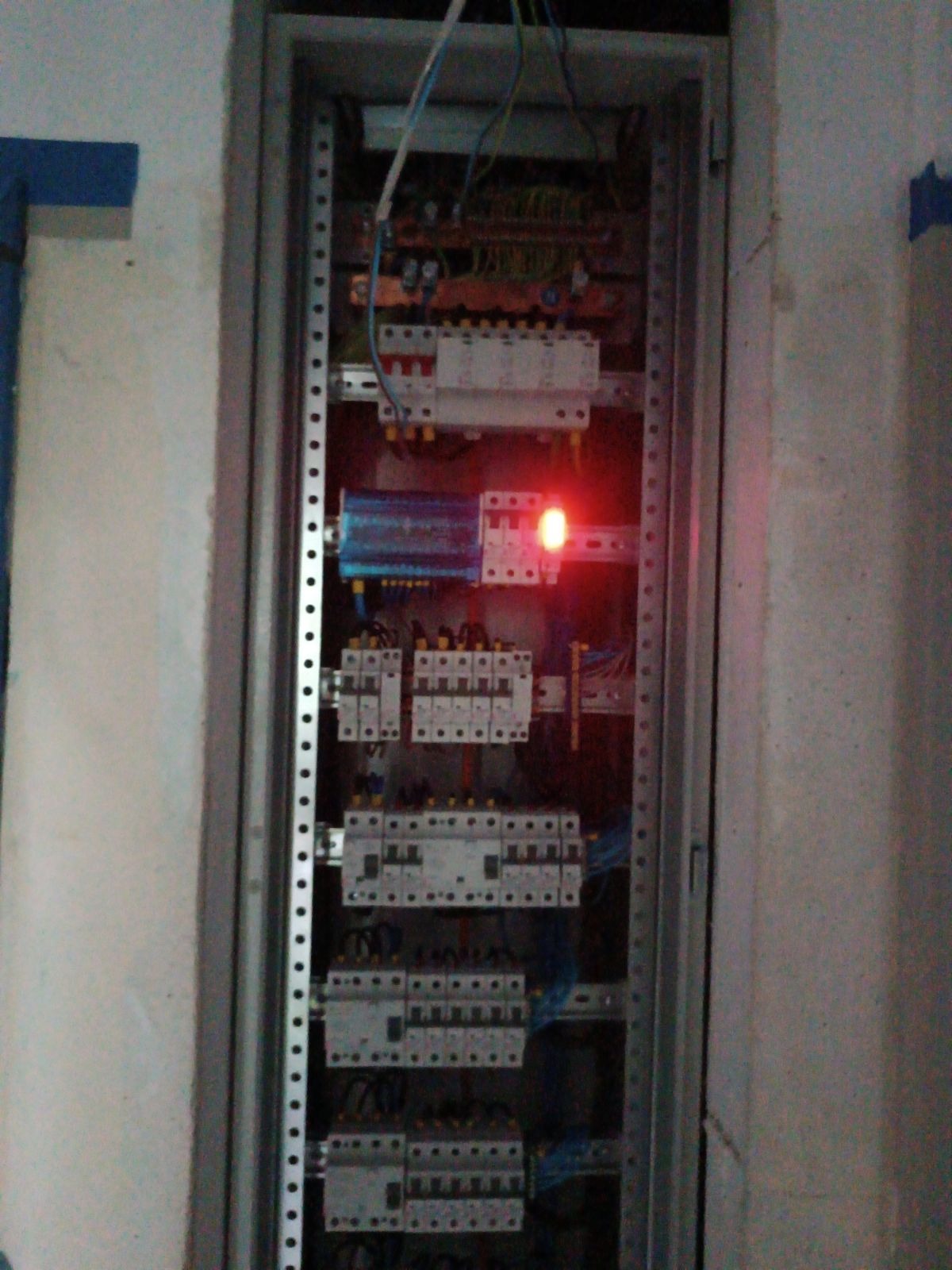 Otwarta skrzynka elektryczna z bezpiecznikami i okablowaniem, widoczna czerwona dioda sygnalizacyjna.