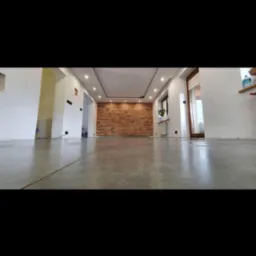 Wnętrze po remoncie z widoczną ścianą z cegły, jasnymi ścianami, wylewką na podłodze i oświetleniem sufitowym.