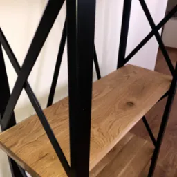 Regał z drewnianymi półkami i czarną metalową konstrukcją w kształcie litery X, widok z dołu na drewniany parkiet.