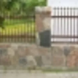 Fragment ogrodzenia z kostki granitowej i metalowych przęseł na tle zieleni.