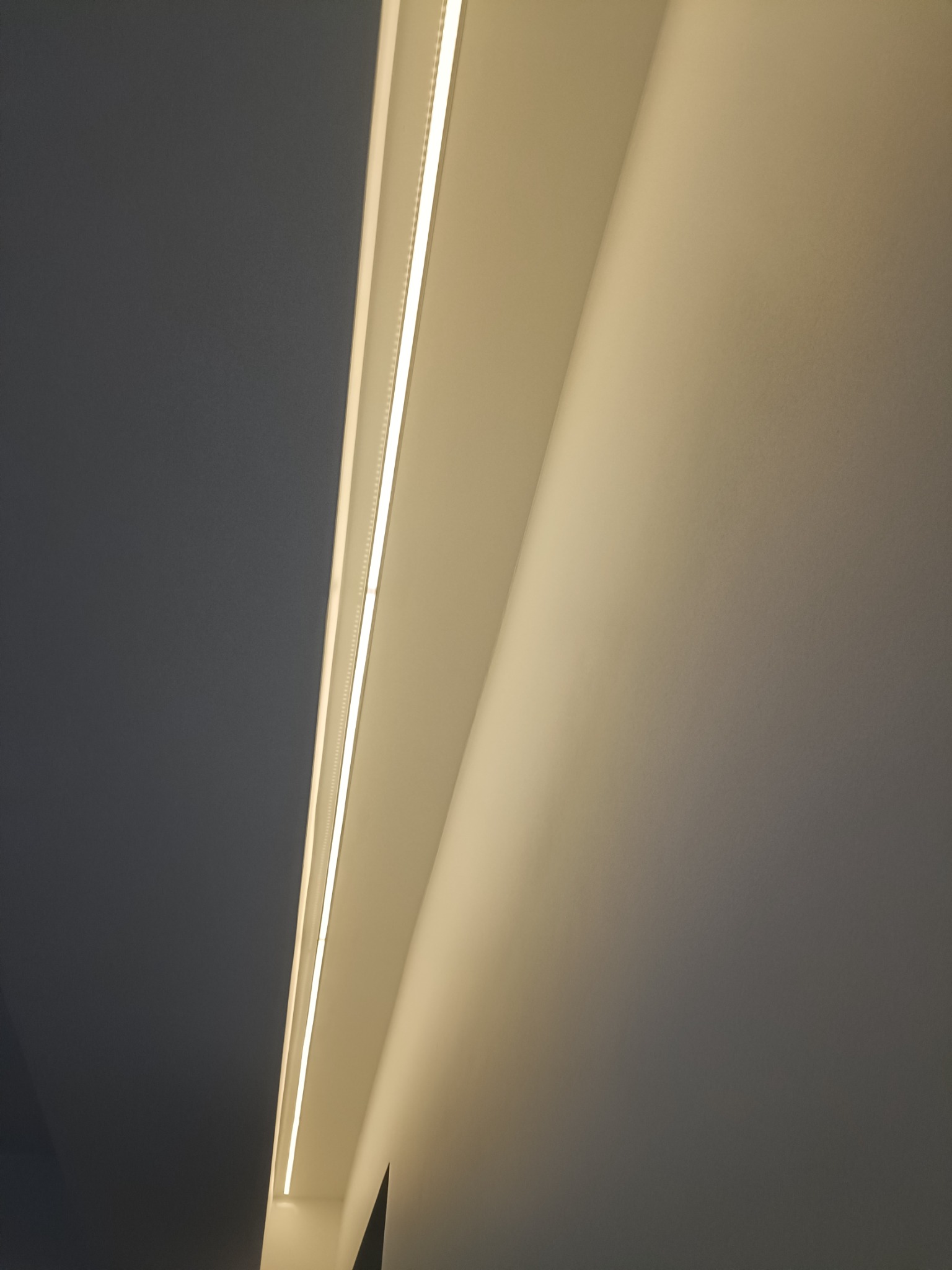 Nowoczesne oświetlenie sufitowe LED w minimalistycznym wnętrzu, z widocznym podziałem na dwie strefy kolorystyczne: ciemnoszarą i kremową.