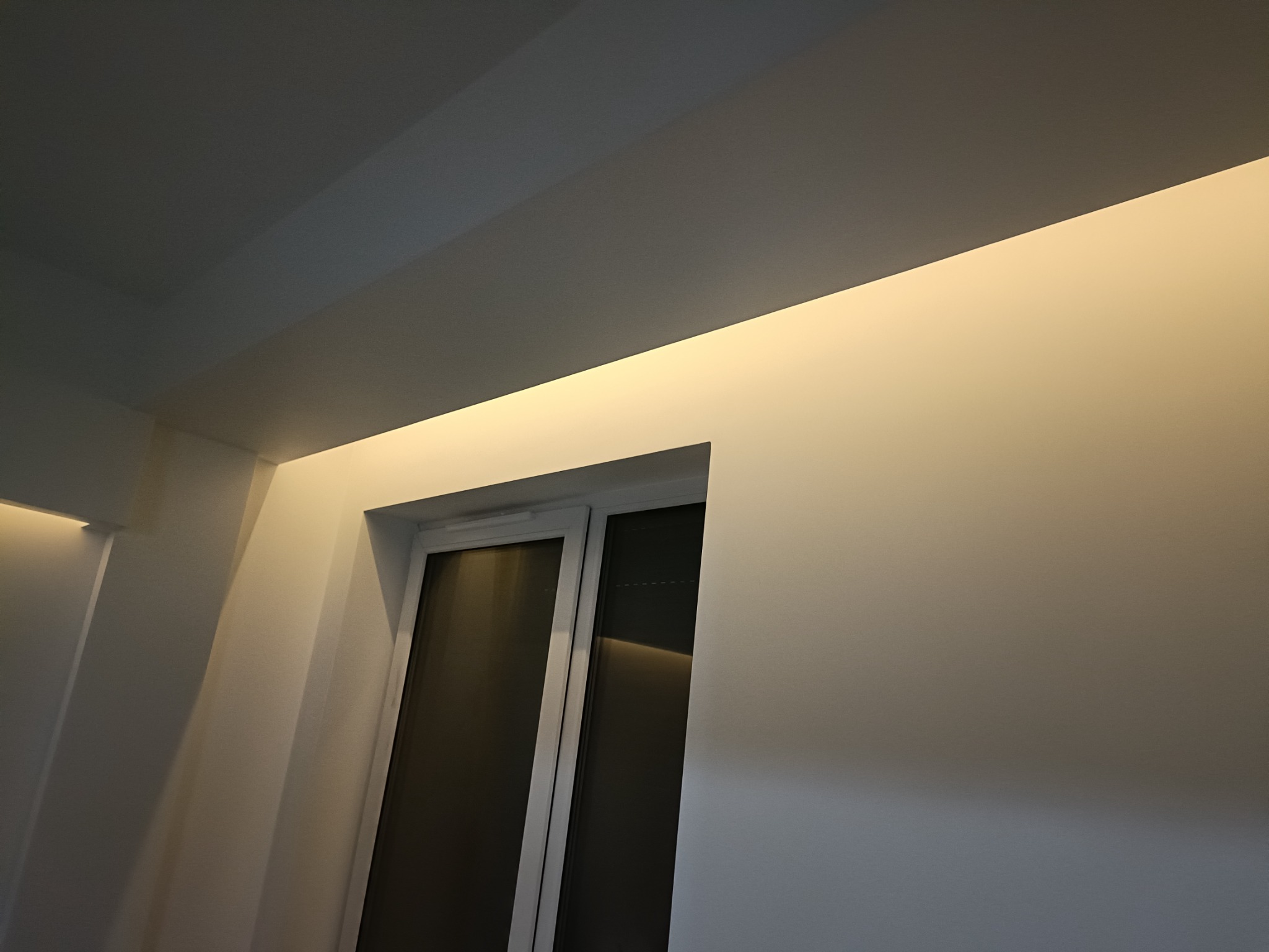 Białe ściany z oświetleniem LED pod sufitem i oknem, widok z dołu, minimalistyczne wnętrze.