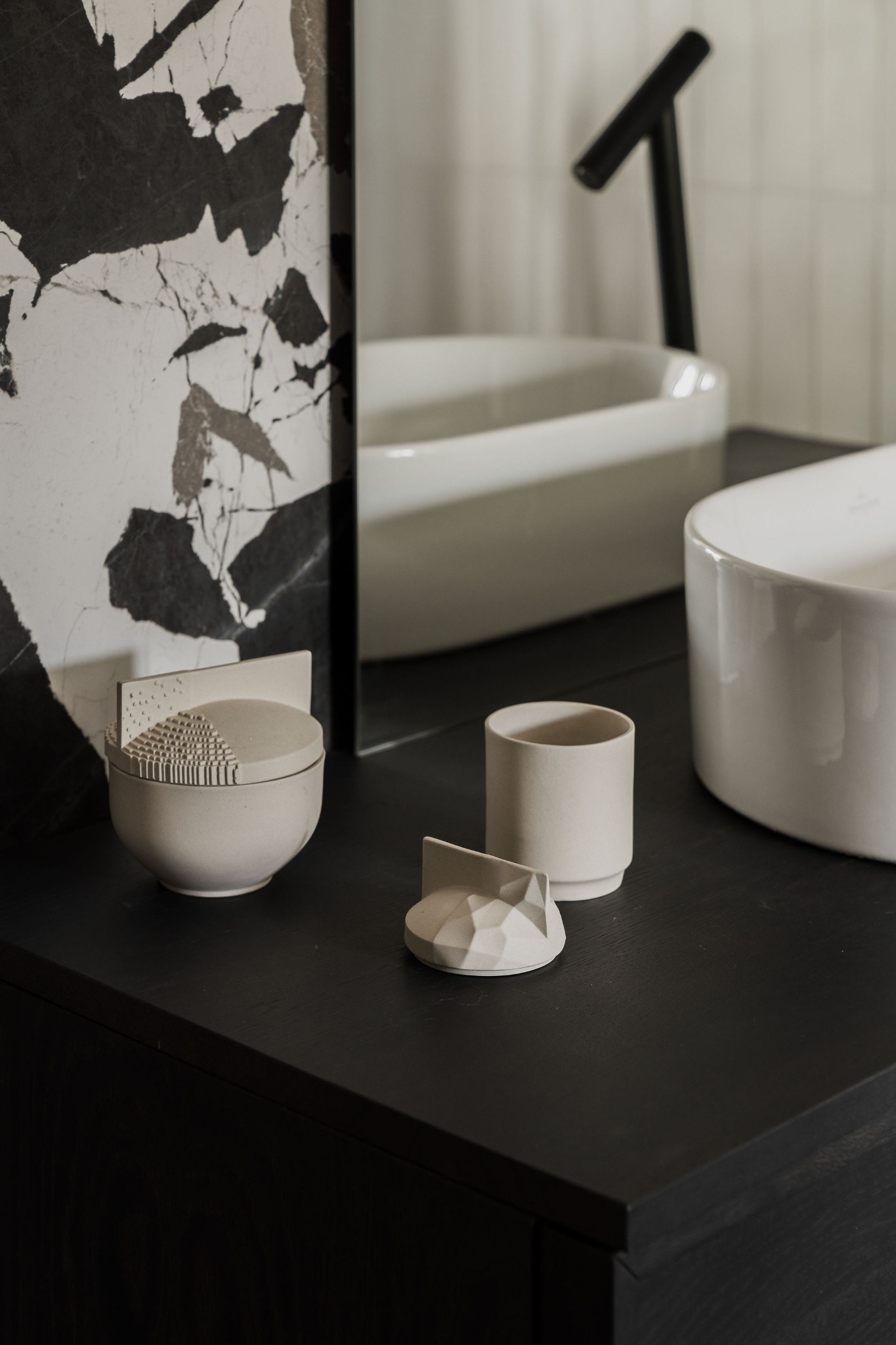 Umywalka nablatowa w minimalistycznej łazience z czarną armaturą i dekoracyjnymi, geometrycznymi akcesoriami łazienkowymi w odcieniach bieli i beżu.