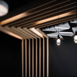 FORMU Mikołaj Małecki - Nowoczesne oświetlenie wnętrza: geometryczny sufit z drewnianych listew, designerskie lampy wiszące z żarówkami Edisona, minimalistyczny styl i ciemne tło.