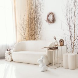 FORMU Mikołaj Małecki - Jasne wnętrze z kremową sofą, dekoracjami z gałęzi, białym królikiem i minimalistycznymi stolikami. Wieniec na ścianie dodaje naturalnego akcentu.