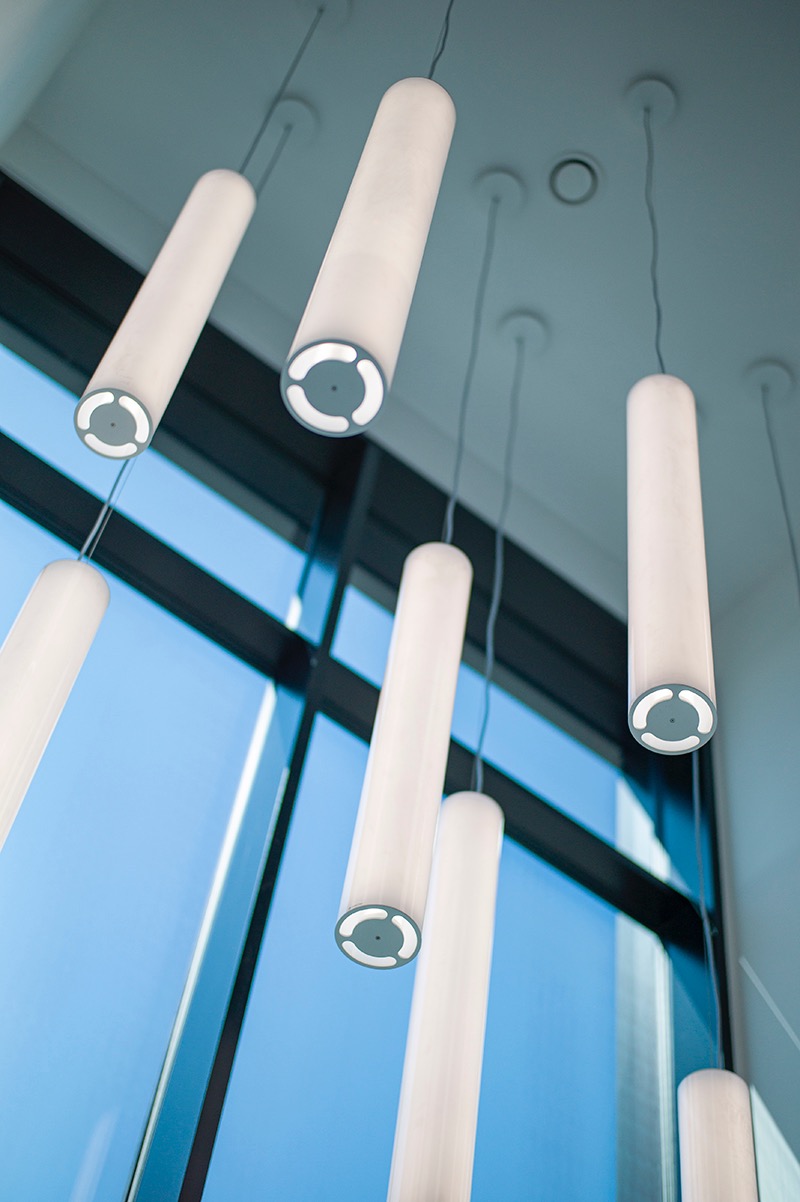 Nowoczesne oświetlenie wnętrza: cylindryczne lampy wiszące z okrągłymi detalami, na tle błękitnego okna. Minimalistyczny design, jasne światło.