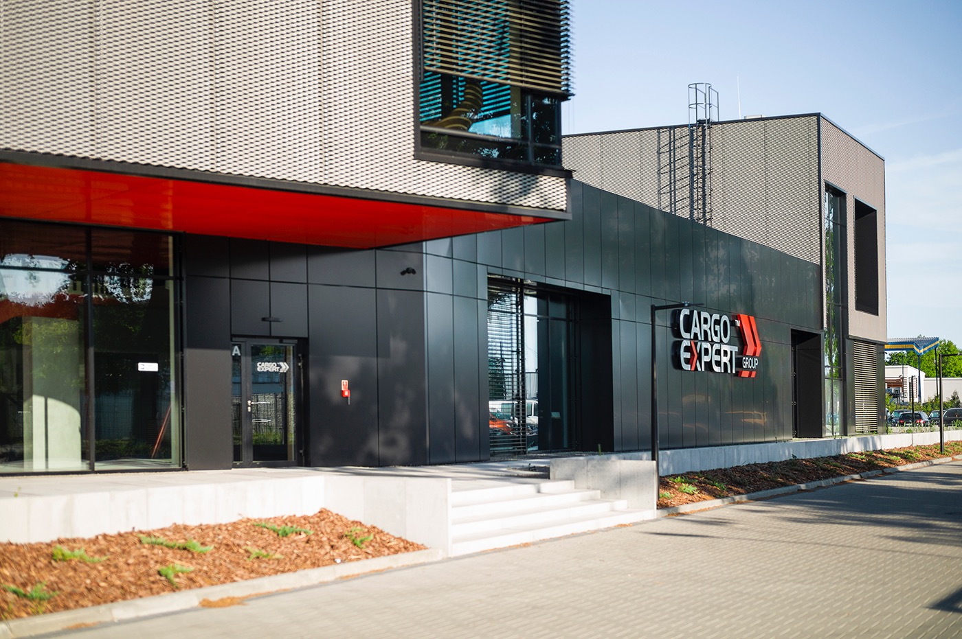 Nowoczesny budynek biurowy z czarną elewacją i logo Cargo Expert Group, widok z zewnątrz, jasne oświetlenie, minimalistyczny design.