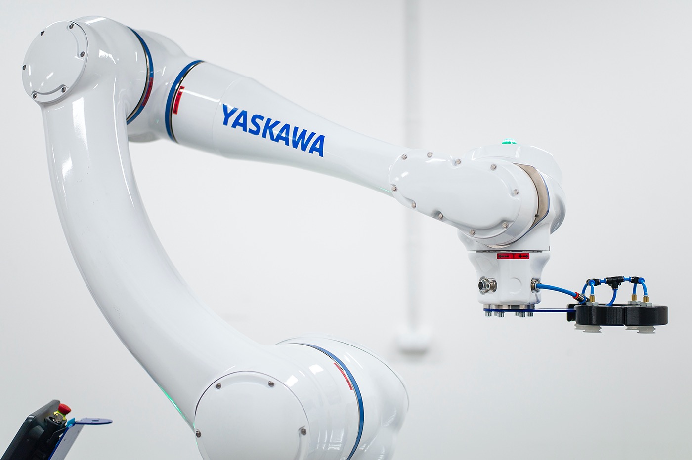 Biały robot przemysłowy Yaskawa z przyssawkami na końcu ramienia, na tle białej ściany.