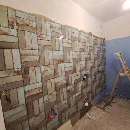 ROBERT KIEŁBASA - Ściana łazienki w trakcie układania płytek w cegiełkę, widoczne krzyżyki dystansowe, instalacja wodna i drabina