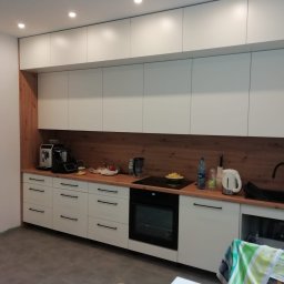 Wojtek Turowski - Nowoczesna kuchnia z białymi szafkami, drewnianym panelem, czarnymi uchwytami i sprzętem AGD na drewnianym blacie.