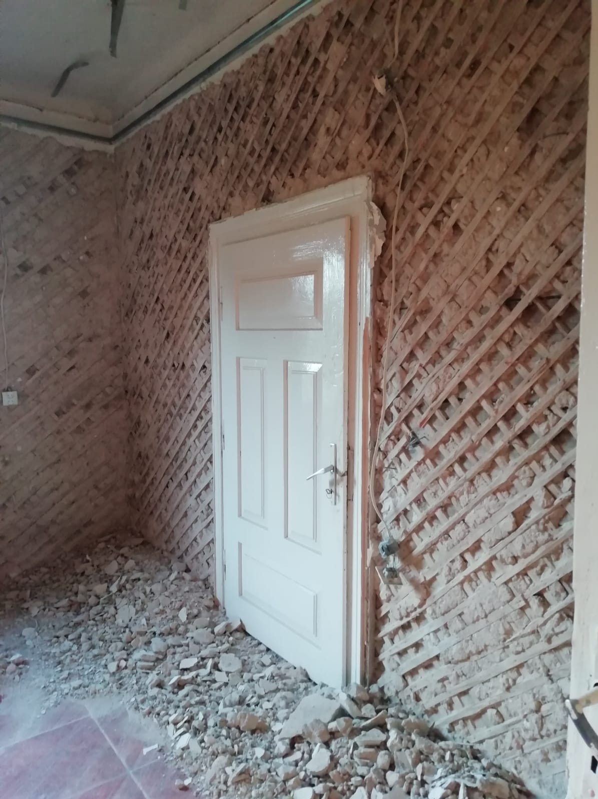 Pokój w trakcie przygotowania do tynkowania: ściany z drewnianą kratownicą, nowa biała ościeżnica i drzwi, gruz na podłodze.