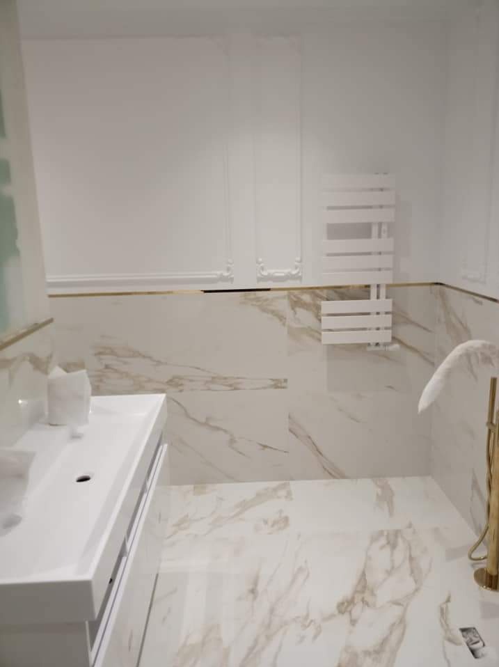 Biała łazienka z marmurowymi płytkami, złotymi akcentami i grzejnikiem drabinkowym