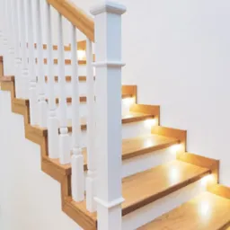 Nowoczesne drewniane schody z białymi balustradami i podświetleniem LED pod każdym stopniem, widok z dołu.