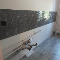 AXVI Usługi Ogólnoremontowe Julia Tubiak - Ściana z dekoracyjną płytką imitującą marmur nad instalacją wodną i ułożona podłoga z płytek imitujących drewno.