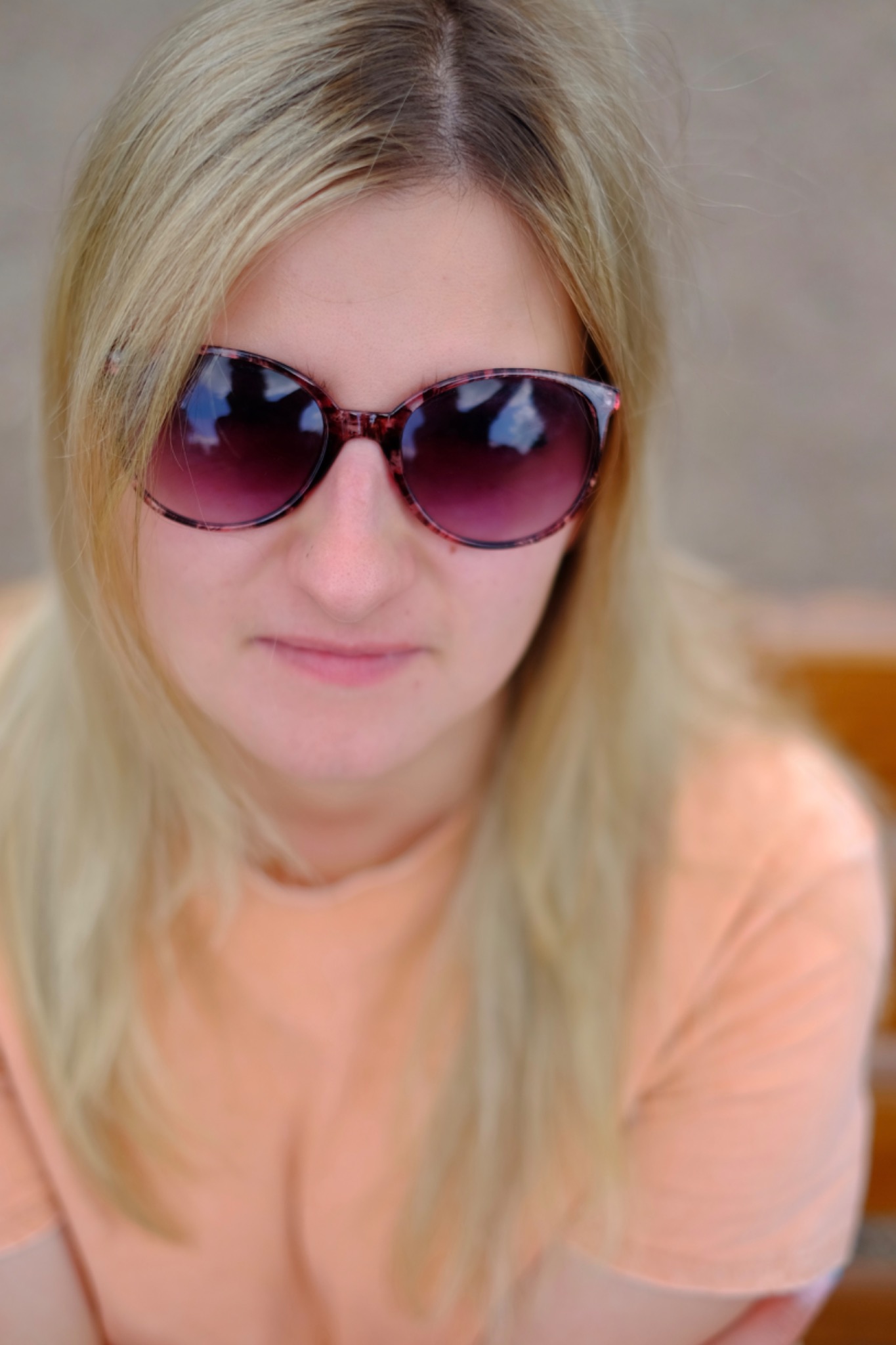 Portret blondynki w okularach przeciwsłonecznych z odbiciem nieba, ujęcie z góry, delikatne rozmycie tła.