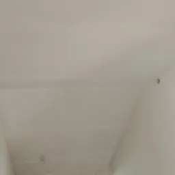 Biały sufit po szpachlowaniu, widoczne niedoskonałości i łączenia płyt kartonowo-gipsowych, przygotowany do dalszych prac wykończeniowych, małe okno w tle.