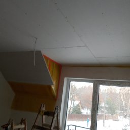 Usługi remontowo budowlane - Montaż płyty gipsowo-kartonowej na poddaszu, widoczne rusztowanie, okno balkonowe z widokiem na zimowy krajobraz.