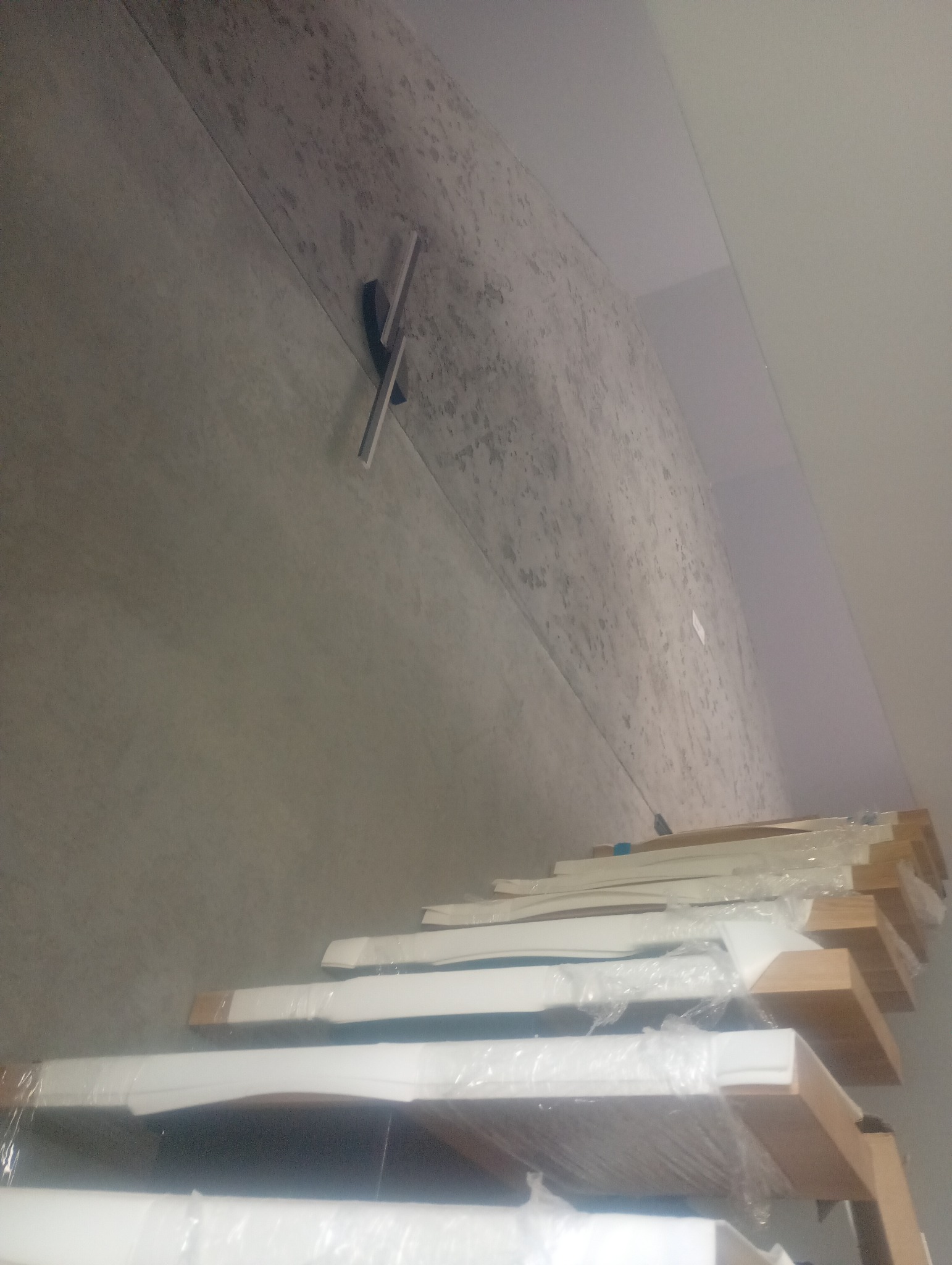 Szare wykończenie ściany z nowoczesnym zegarem i ułożonymi panelami podłogowymi w folii, czekającymi na montaż. Widok z dołu, perspektywa zniekształcona.