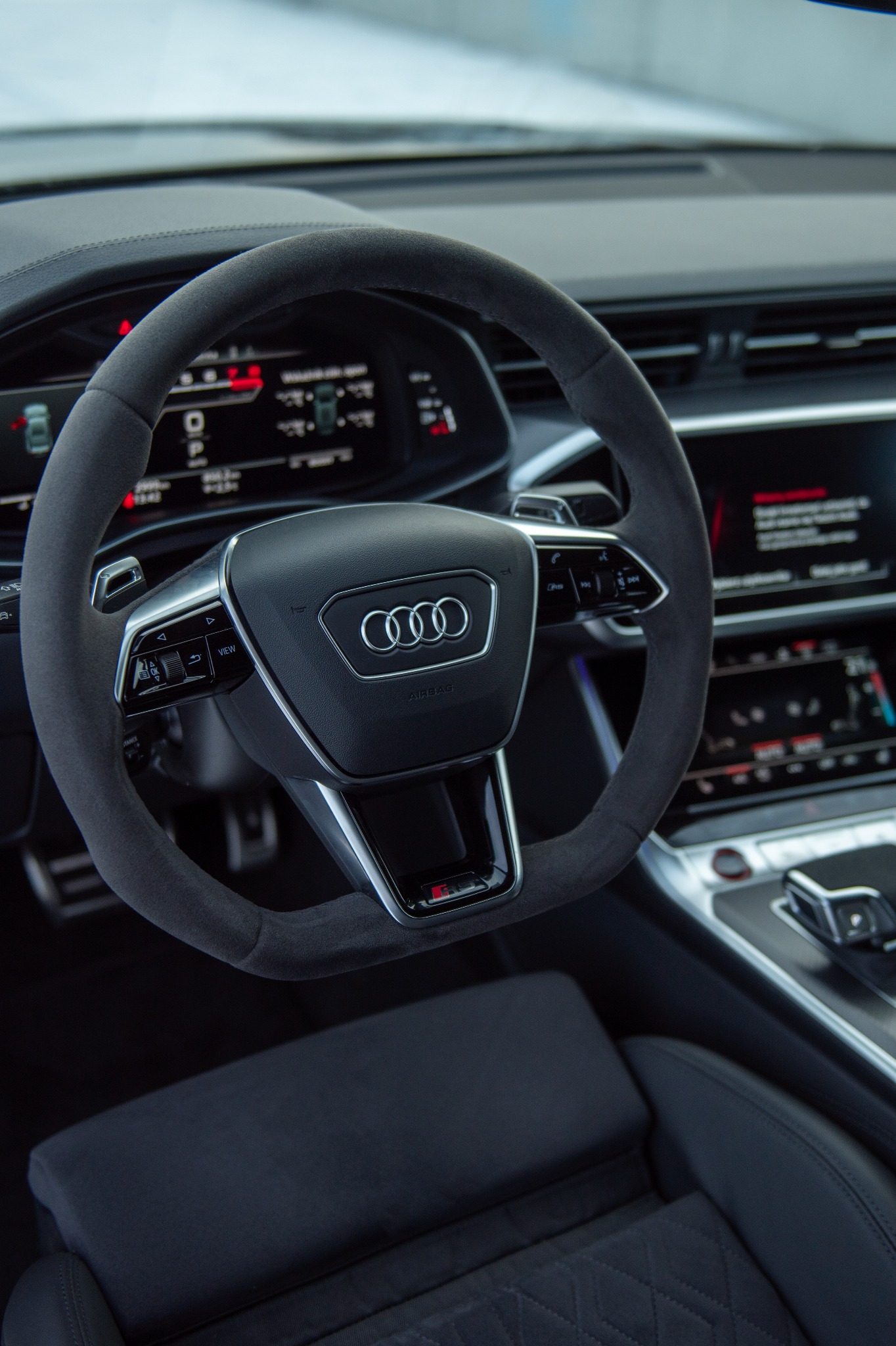 Szczegółowe ujęcie wnętrza samochodu Audi z kierownicą obszytą alcantarą, widoczne cyfrowe zegary i elementy deski rozdzielczej