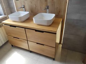 Drewniana szafka łazienkowa z czterema szufladami i dwoma białymi umywalkami nablatowymi, minimalistyczne baterie, jasne drewno na ścianie w tle.