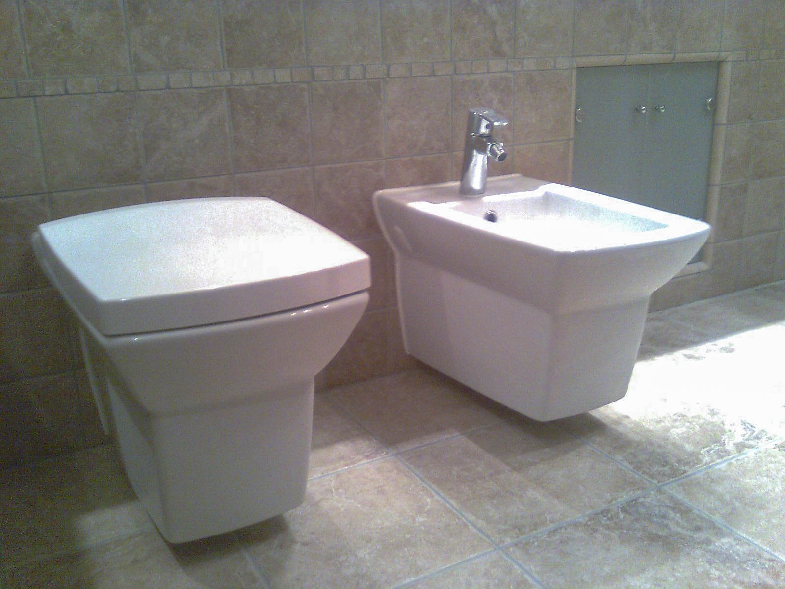 Nowoczesna toaleta i bidet o kwadratowych kształtach, zamontowane na ścianie, z kafelkami w tle.