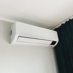 HVAC Business - Biała jednostka wewnętrzna klimatyzacji Samsung WindFree zamontowana na ścianie, widoczne ciemnozielone zasłony w tle.
