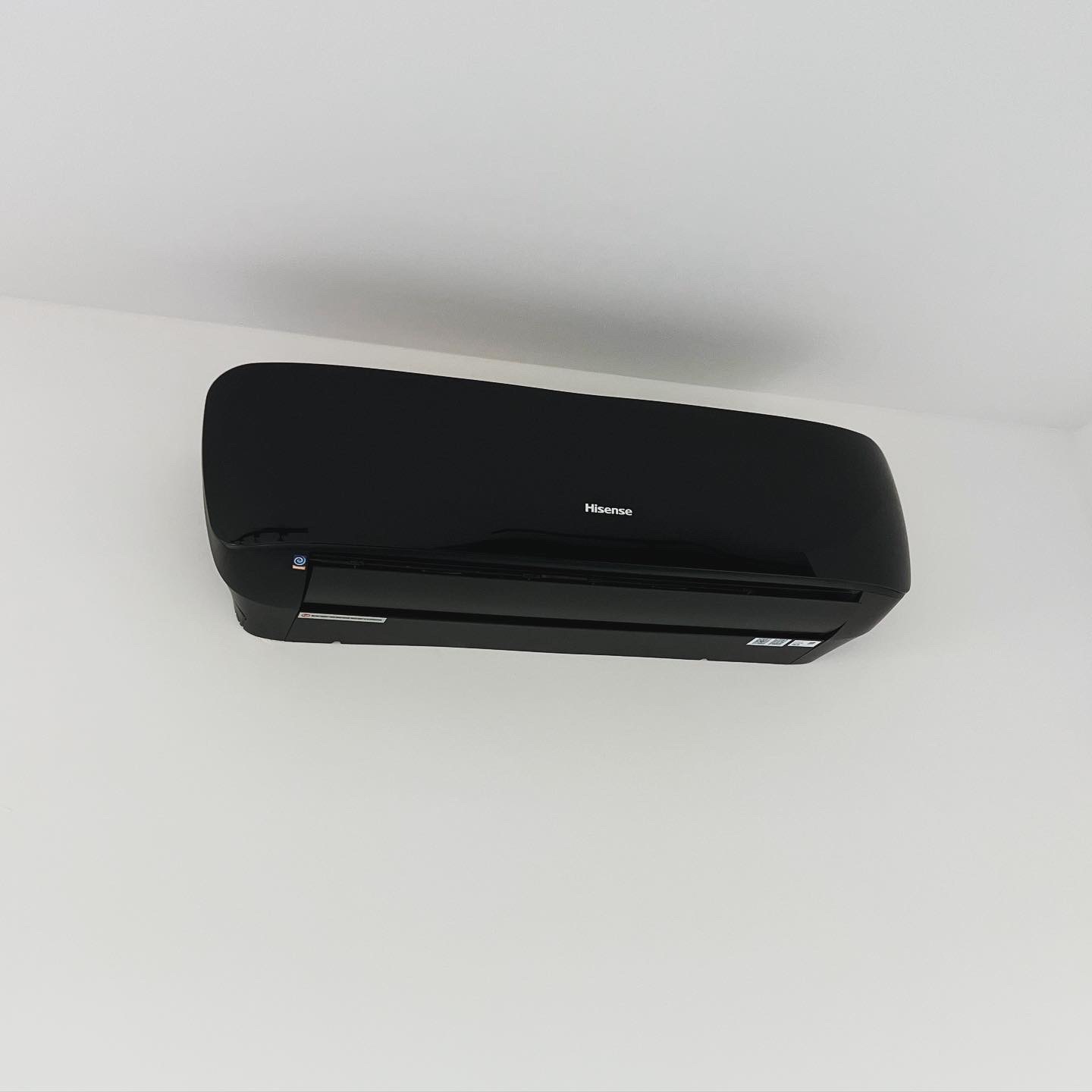 Czarna klimatyzacja Hisense zamontowana na białej ścianie, widok od dołu, minimalistyczny design.