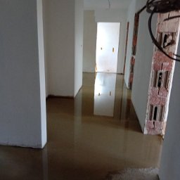 EG - Wnętrze w trakcie prac przygotowawczych do wykończenia: wylewka podłogowa, surowe ściany z widoczną konstrukcją z cegieł i przewodami elektrycznymi.