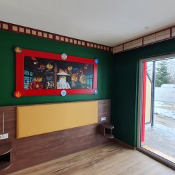NewHome - Pokój tematyczny z zielonymi ścianami, dekoracyjną bordiurą, łóżkiem z drewnianym wezgłowiem i żółtym panelem oraz dużym obrazem Lego Ninjago w czerwonej ramie.