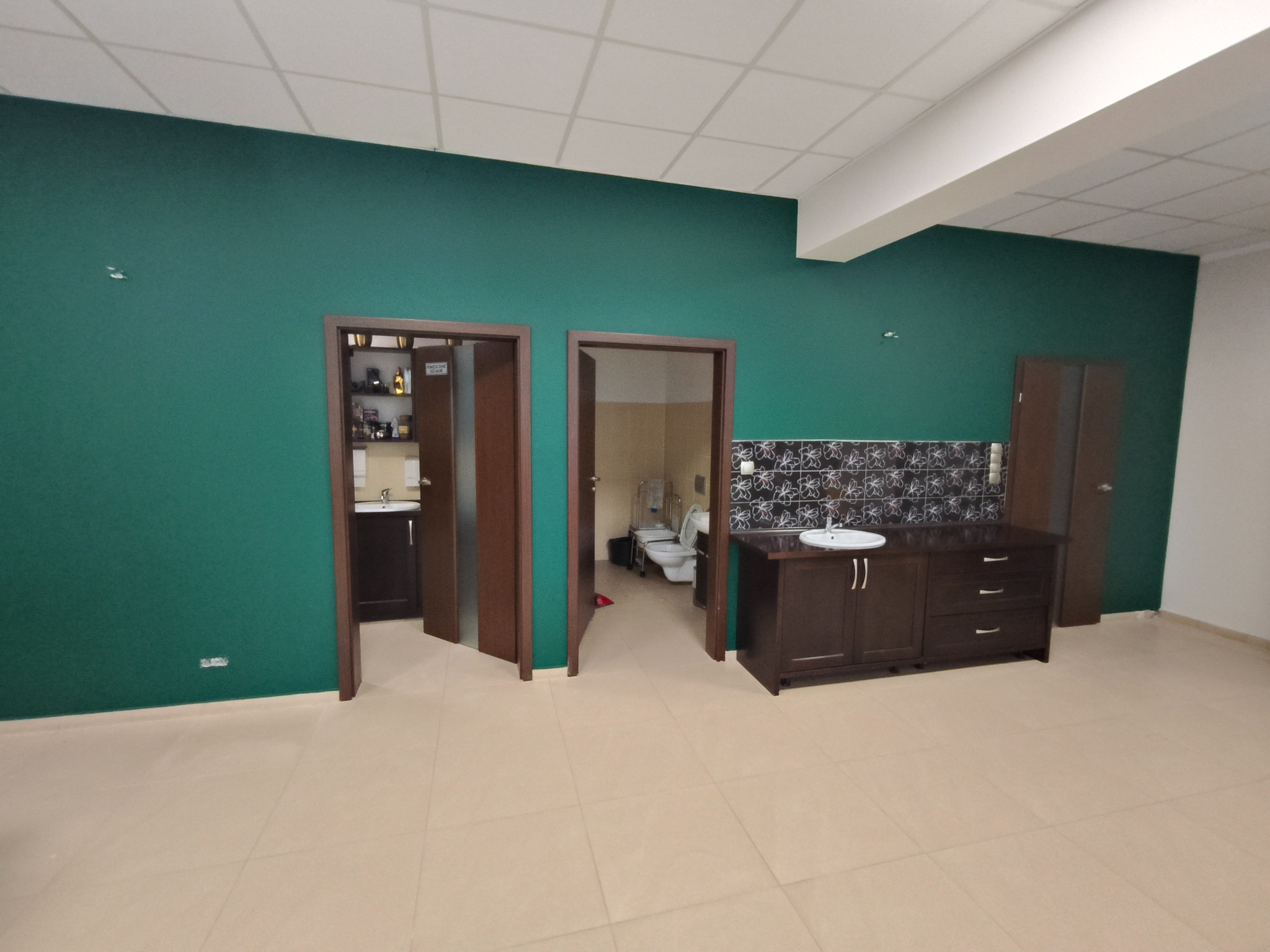Wnętrze po remoncie: ściany pomalowane na ciemnozielony kolor, beżowa podłoga z płytek, dwie łazienki z ciemnobrązowymi szafkami pod umywalki widoczne przez otwarte drzwi.